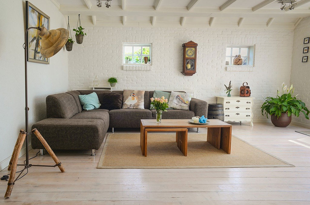 Salón amueblado con sofá tapizado, una lámpara de pie, dos mesas auxiliares y una cómoda 